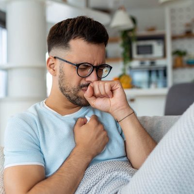 Sick man holding his chest in pain while coughing in the living room. Sore throat and cough, man with lung pain at home, health problems concept